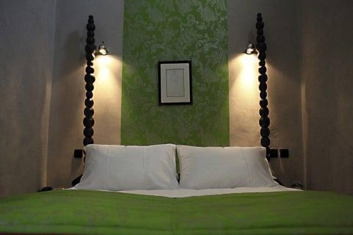 Una cama con una colcha verde, dos lámparas de pared y un cuadro en la pared.