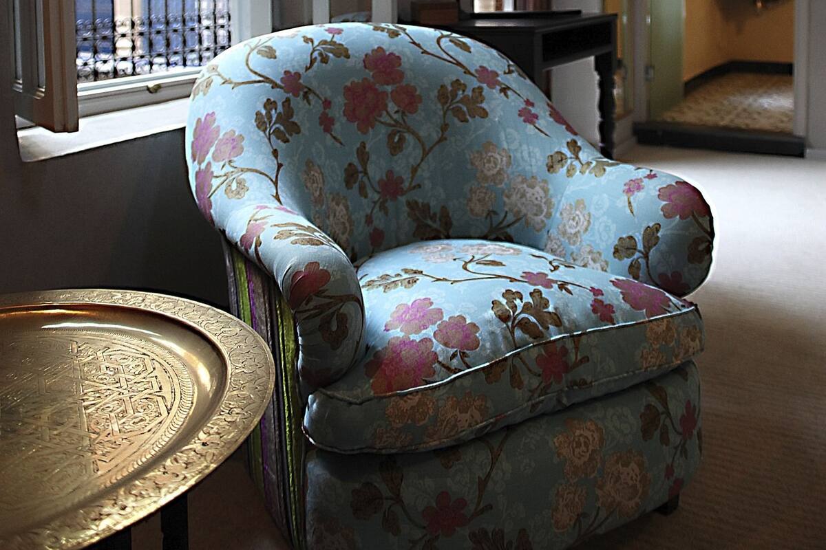Una habitación con un sillón floral, una mesita con una bandeja y vistas a un balcón con barandilla.