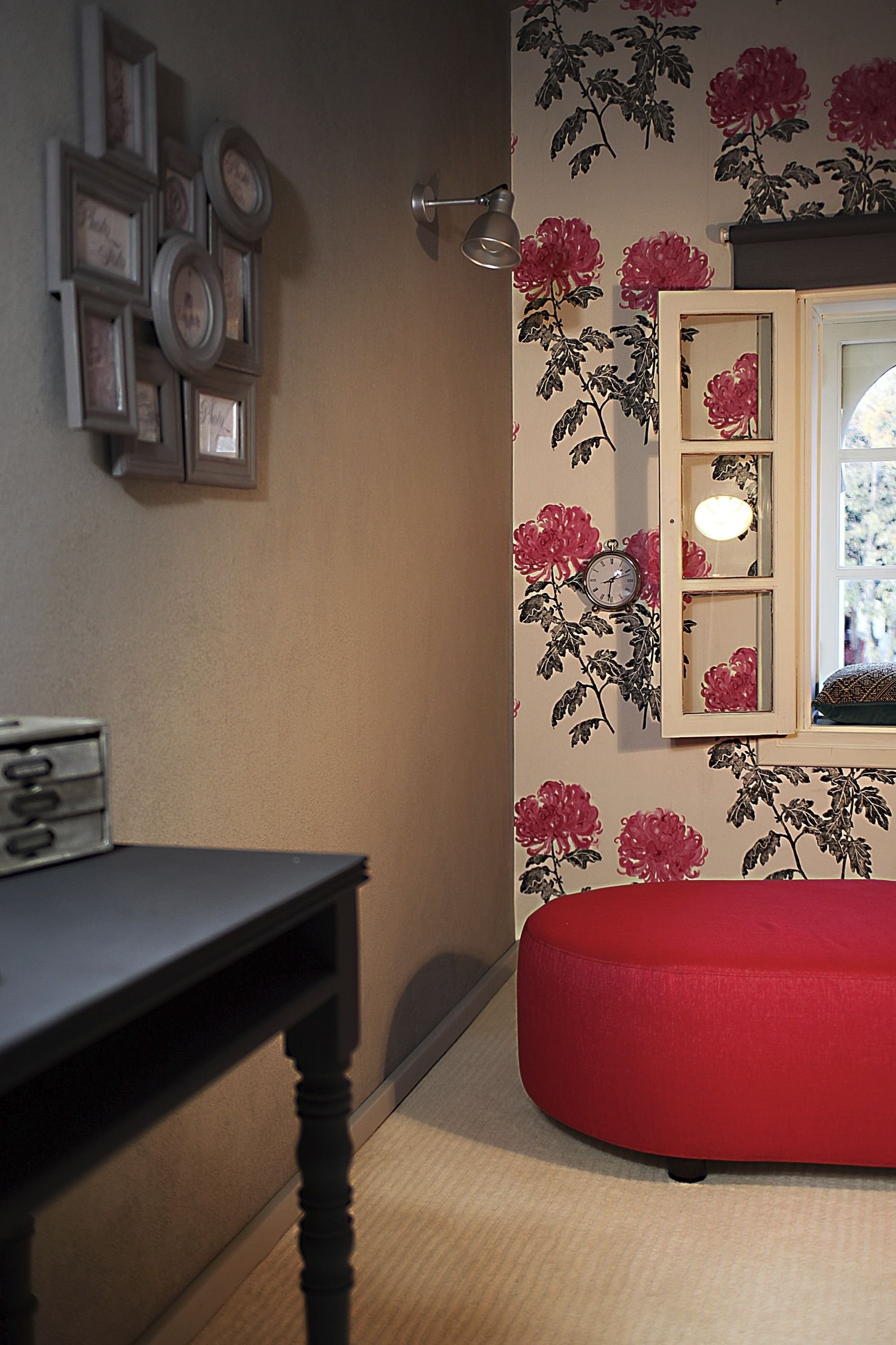 A room with a red ottoman, a wall clock, and framed pictures.