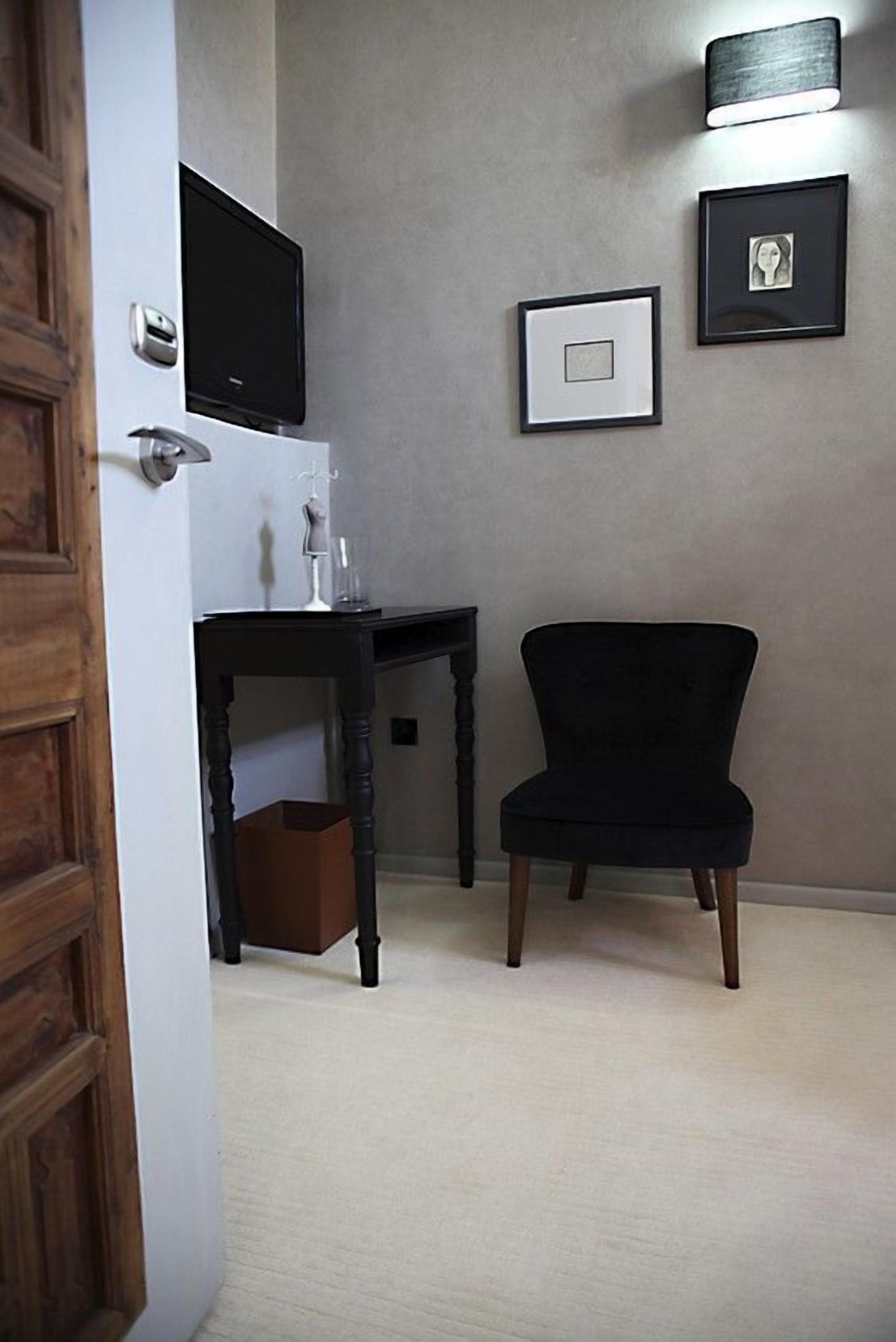 A room with a wooden door, a black chair, a small table, and a wall-mounted TV.