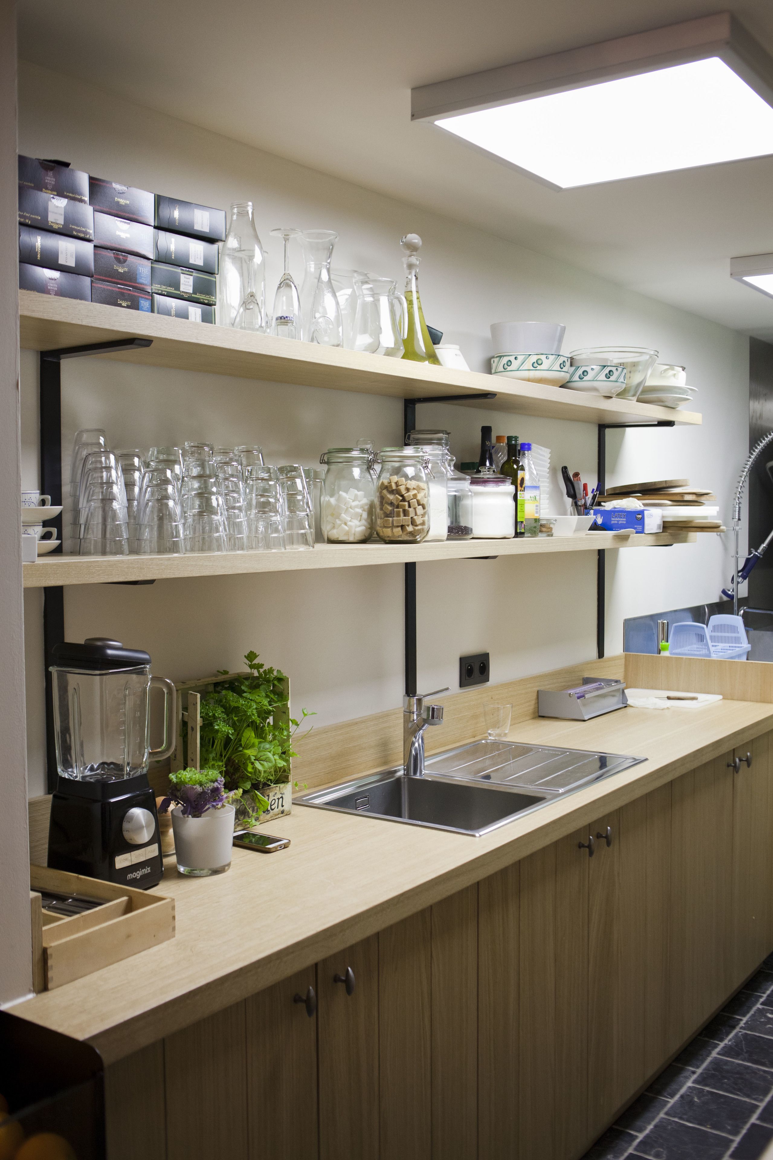 A modern kitchen with wooden cabinets, a countertop, a sink, and various kitchen items like glassware and jars.