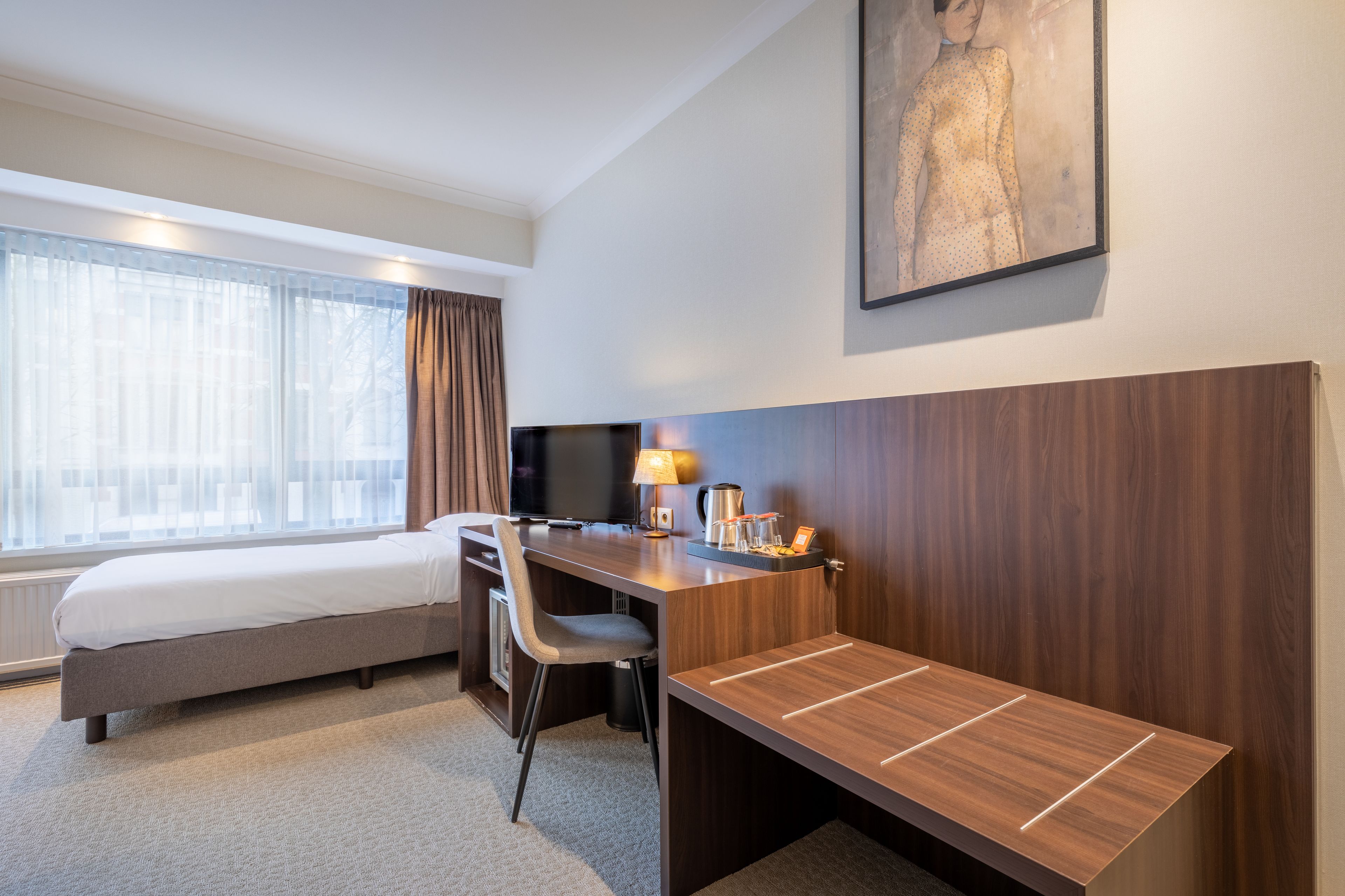 Habitación de hotel con cama, escritorio, silla y un ventanal con cortinas.