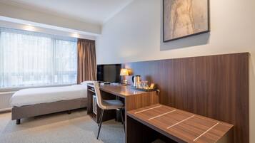Habitación de hotel con cama, escritorio, silla y un ventanal con cortinas.