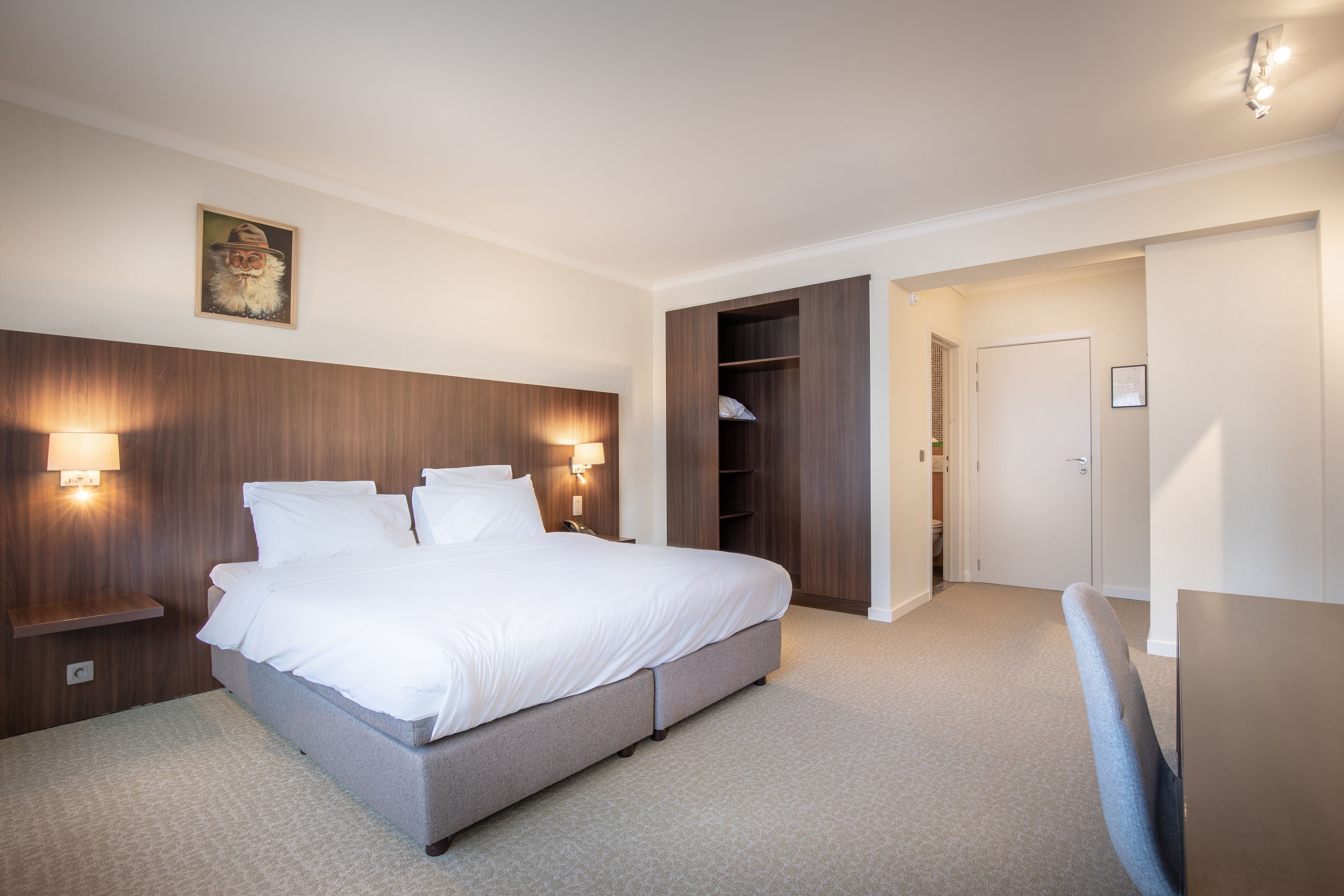 Quarto bem arrumado com cama grande, luminárias de cabeceira, cabeceira de madeira e armário com prateleiras.
