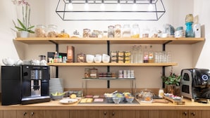 Una barra de desayuno con una máquina de café, una estación de té y diversos alimentos y condimentos.