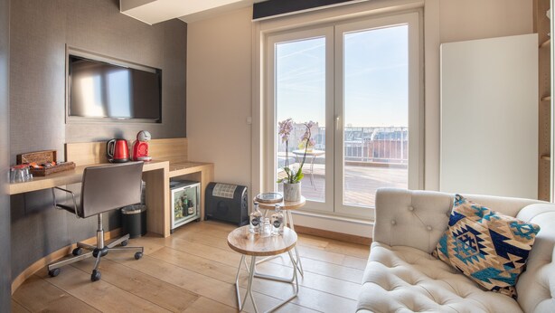 Una sala moderna con un sofá, una mesa de centro, un televisor, un escritorio con una silla y un ventanal con vistas a la ciudad.
