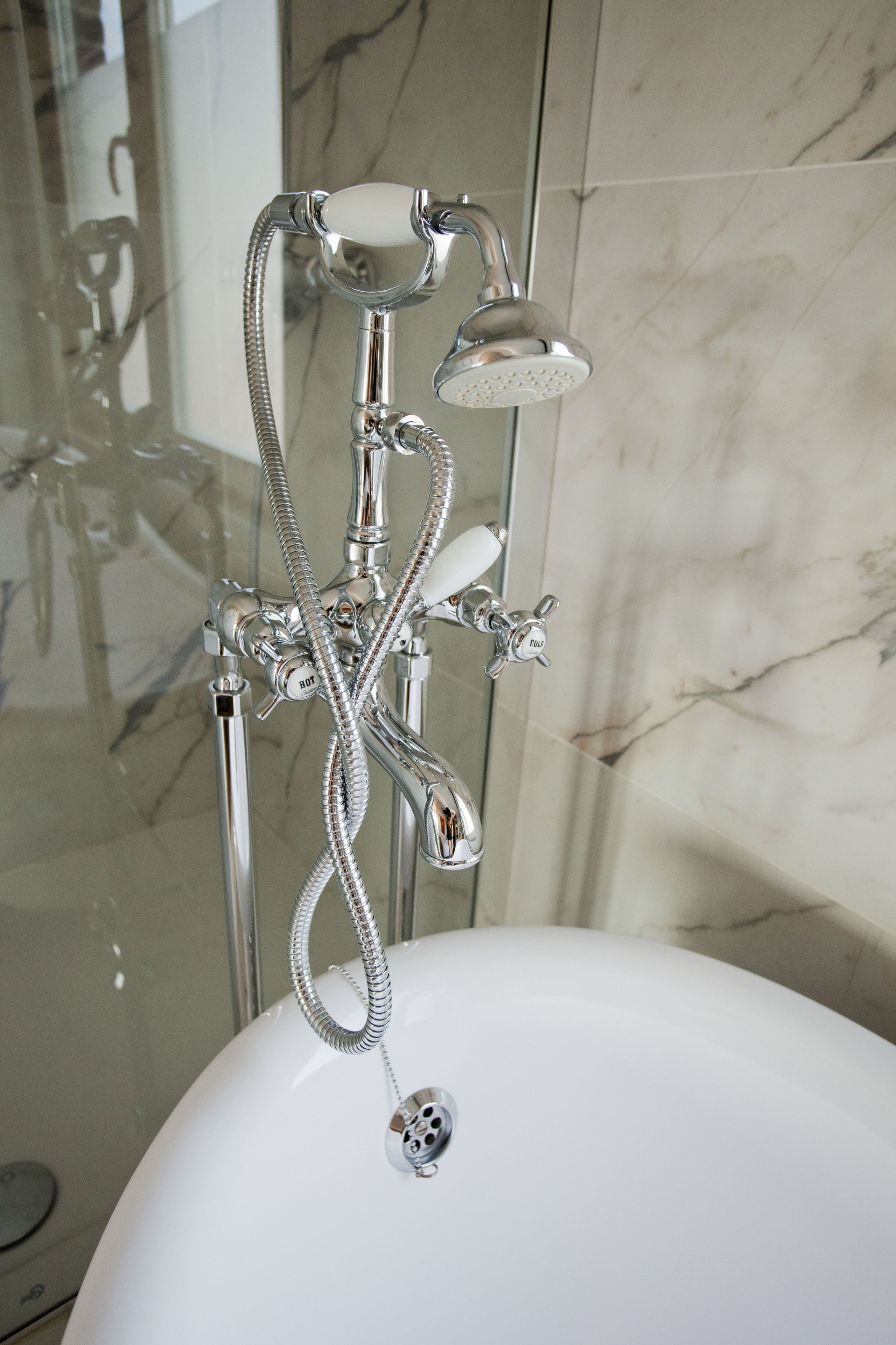 A bathroom with a chrome shower head, a handheld shower attachment, and a wall-mounted faucet.