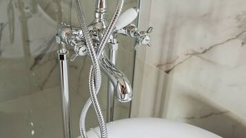 A bathroom with a chrome shower head, a handheld shower attachment, and a wall-mounted faucet.