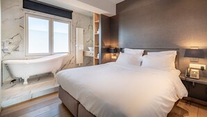 Una habitación de hotel moderna con una cama grande, una bañera integrada, paredes de mármol y un teléfono junto a la cama.