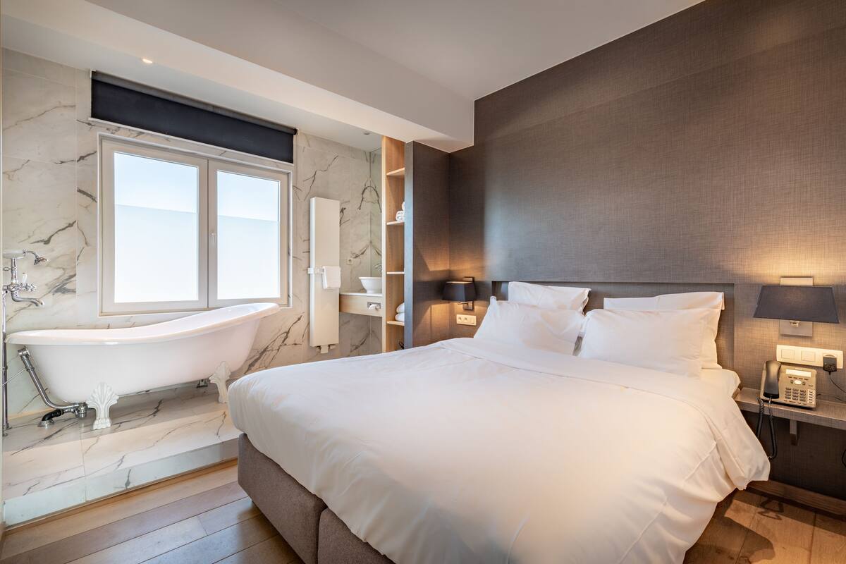 Ein modernes Hotelzimmer mit einem großen Bett, einer integrierten Badewanne, Marmorwänden und einem Nachttischtelefon.