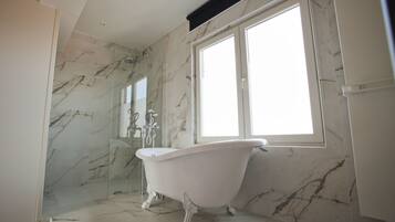 A bathroom with a freestanding bathtub, marble walls, and a large window providing natural light.