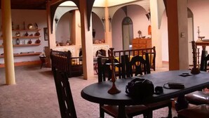 A dining area with a round table, chairs, and a wooden bench. There are shelves with various items in the background. - Douar des Oliviers (Ounagha)