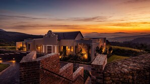 A modern house with a stone wall and brick entrance, surrounded by a landscaped garden and a view of distant hills. - Delaire Graff Lodges & Spa (Stellenbosch)