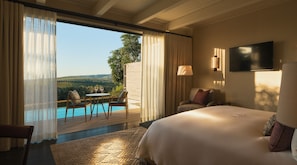 Une chambre d’hôtel équipée d’un lit, d’une télévision, donnant sur la piscine, et comprenant un coin repas avec des chaises et une table.