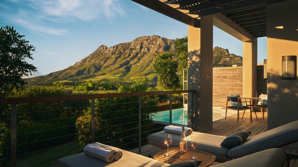 A balcony with a view of mountains, a pool, and a seating area with cushions and a table. - Delaire Graff Lodges & Spa (Stellenbosch)