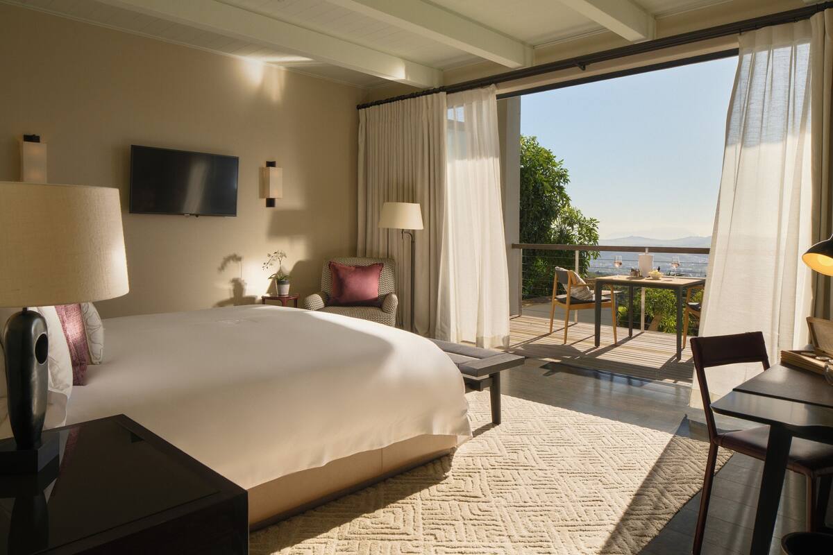 Quarto de hotel com uma cama grande, televisão, escrivaninha e varanda com vista.