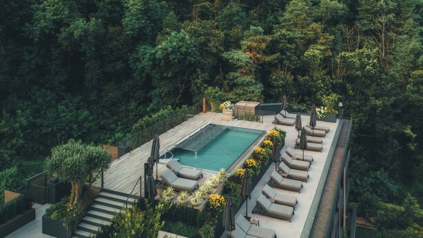Una piscina en la azotea con sillones de descanso y una escalera que conduce a una terraza rodeada de exuberante vegetación y montañas al fondo.