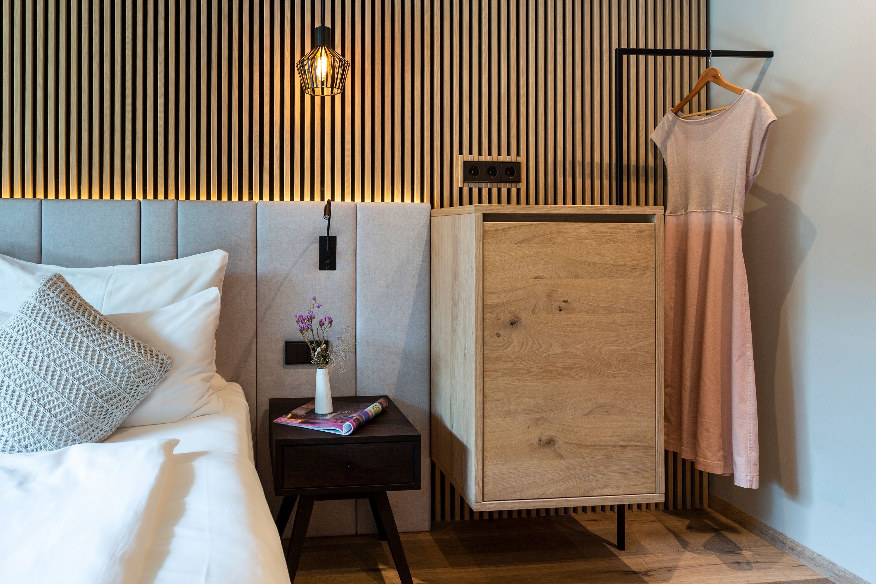 Un dormitorio moderno con cama, mesita de noche, cómoda y un vestido colgado.