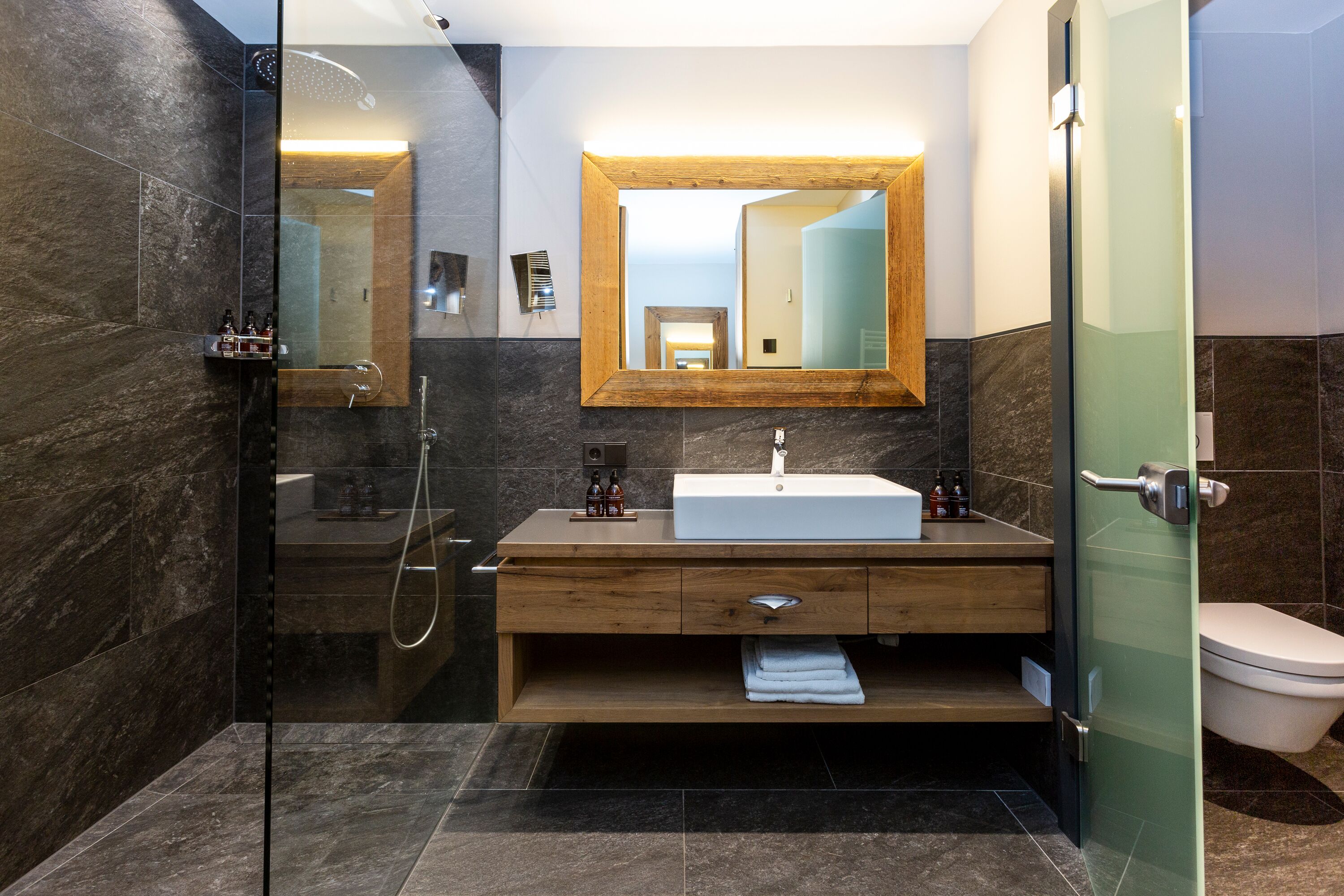 A modern bathroom with a glass-enclosed shower, a wooden vanity with a sink, and a large mirror above the vanity.