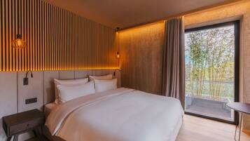 Habitación de hotel moderna con una cama grande, una mesita de noche, una pequeña mesa junto a la ventana y vistas a zonas verdes.