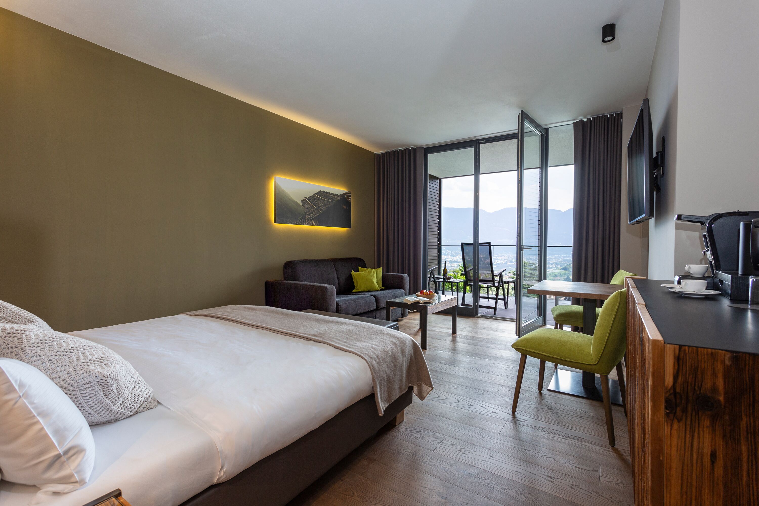 A hotel room with a bed, a sofa, a dining table, and a TV.