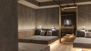 Una habitación moderna y minimalista con un sofá y un banco, ambos con cojines. Hay dos lámparas colgantes y una lámpara de techo.