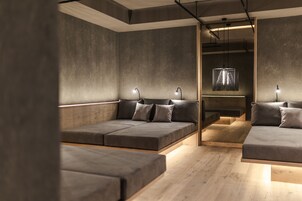 A modern, minimalist room with a sofa and a bench, both with cushions. There are two pendant lights and a hanging light fixture.