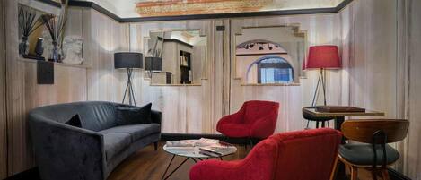 A room with a curved ceiling, a grey sofa, red chairs, a small table, and a lamp.