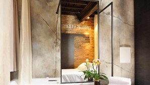 A modern bathroom with a large mirror, a wooden vanity, a black chair, and a potted plant. - Relais Orso (Rome)