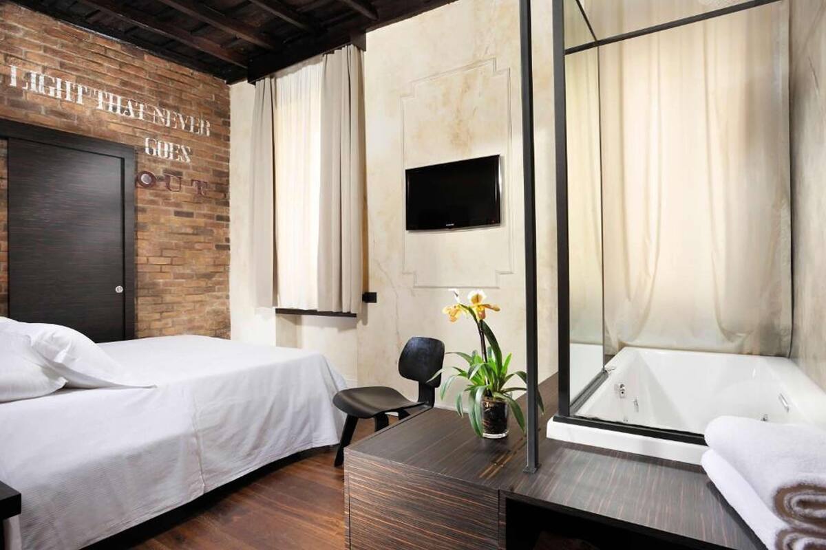 Habitación de hotel con pared de ladrillo, cama, escritorio con planta, silla, televisor y bañera.