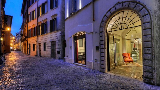 A cobblestone street leading to a building with a large arched entrance and a visible interior with a chair and table. - Relais Orso (Rome)