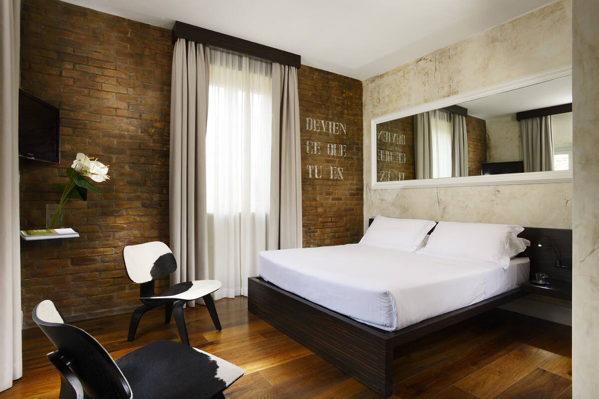 Un dormitorio moderno con pared de ladrillo, una cama, una silla, un escritorio y un espejo.