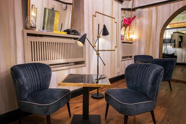 Une pièce comprenant deux fauteuils à revêtement bleu foncé, une table avec un plateau en verre, un lampadaire et un miroir au mur.