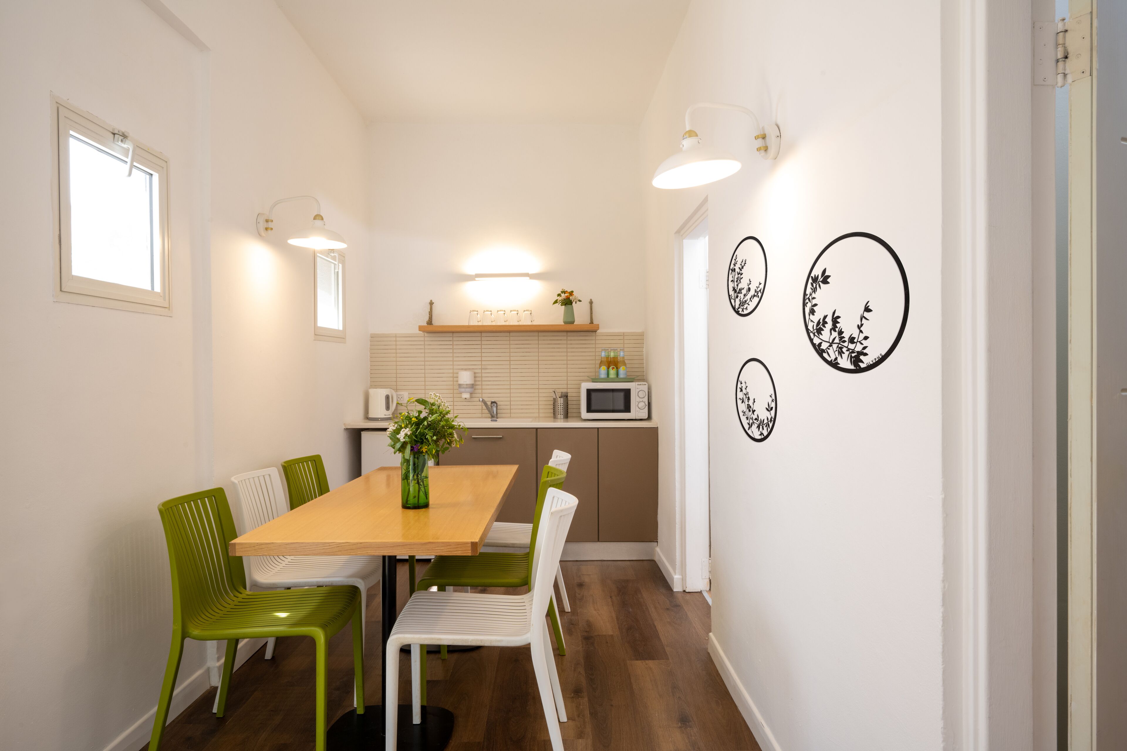 A compact kitchen with a wooden table, green and white chairs, a microwave, and a shelf with kitchen items.
