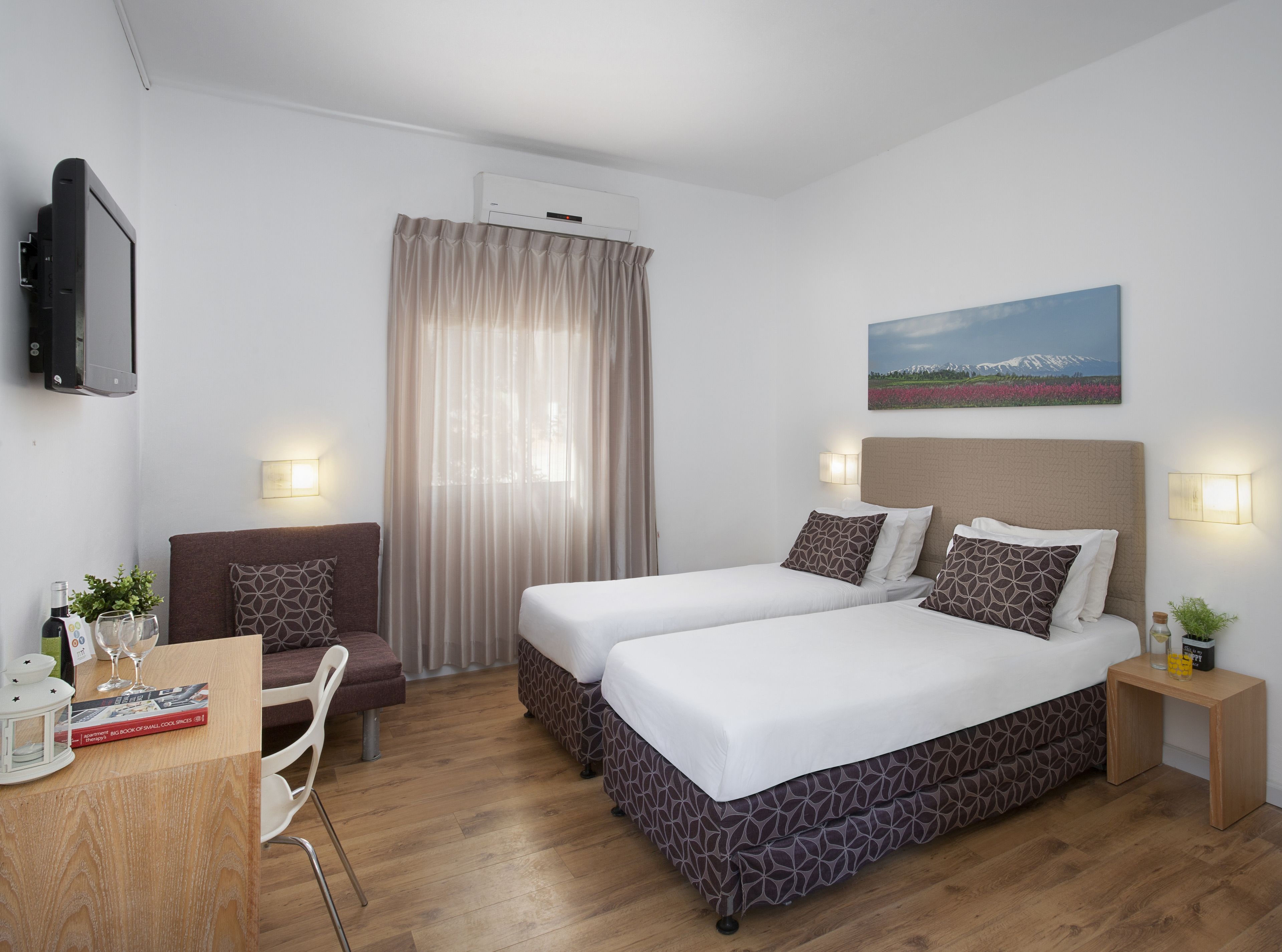 Habitación de hotel con dos camas, un escritorio, una silla, un televisor y un cuadro en la pared.