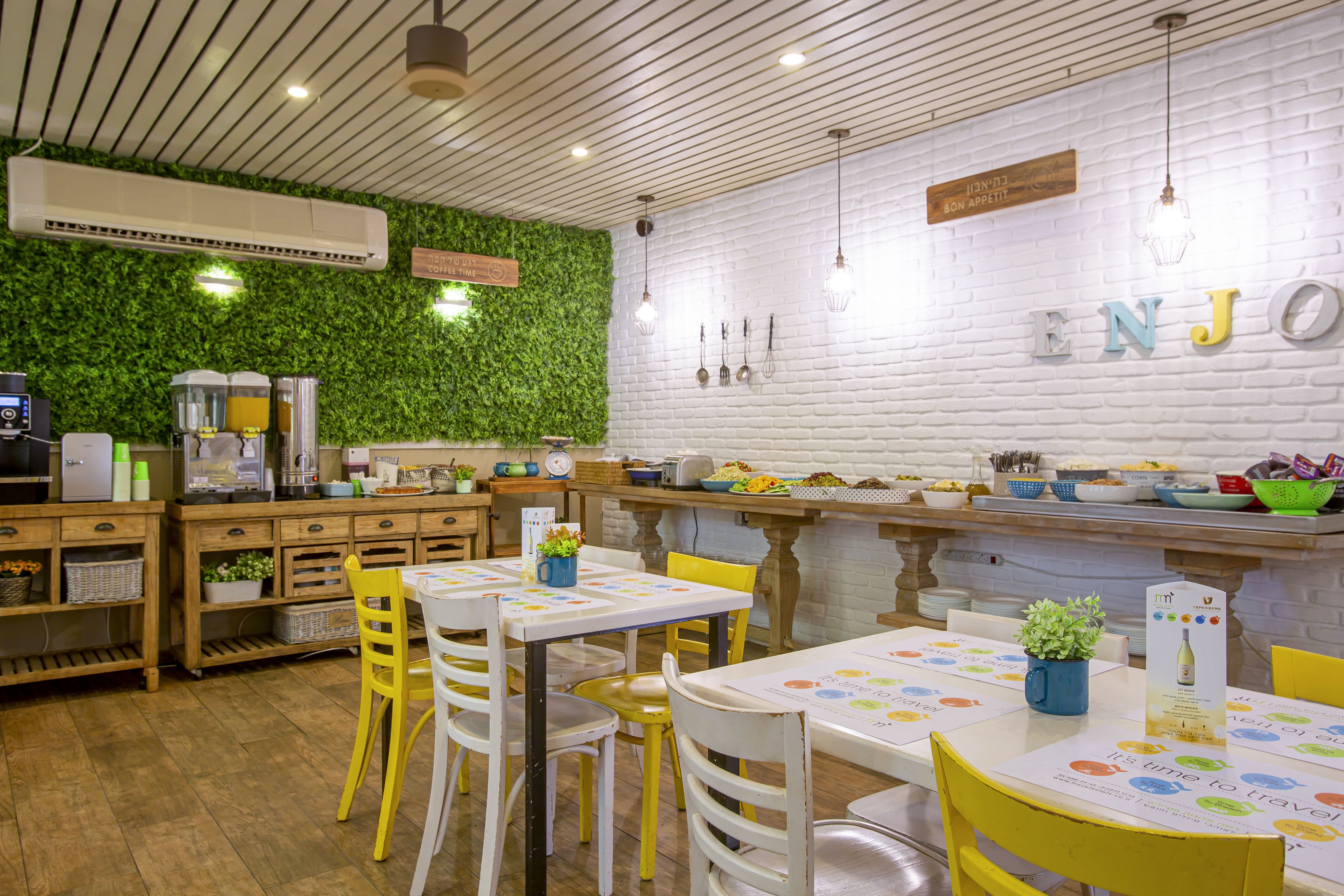 A restaurant with wooden tables and chairs, a green wall, and a white brick wall with the word "ENJOY" on it.