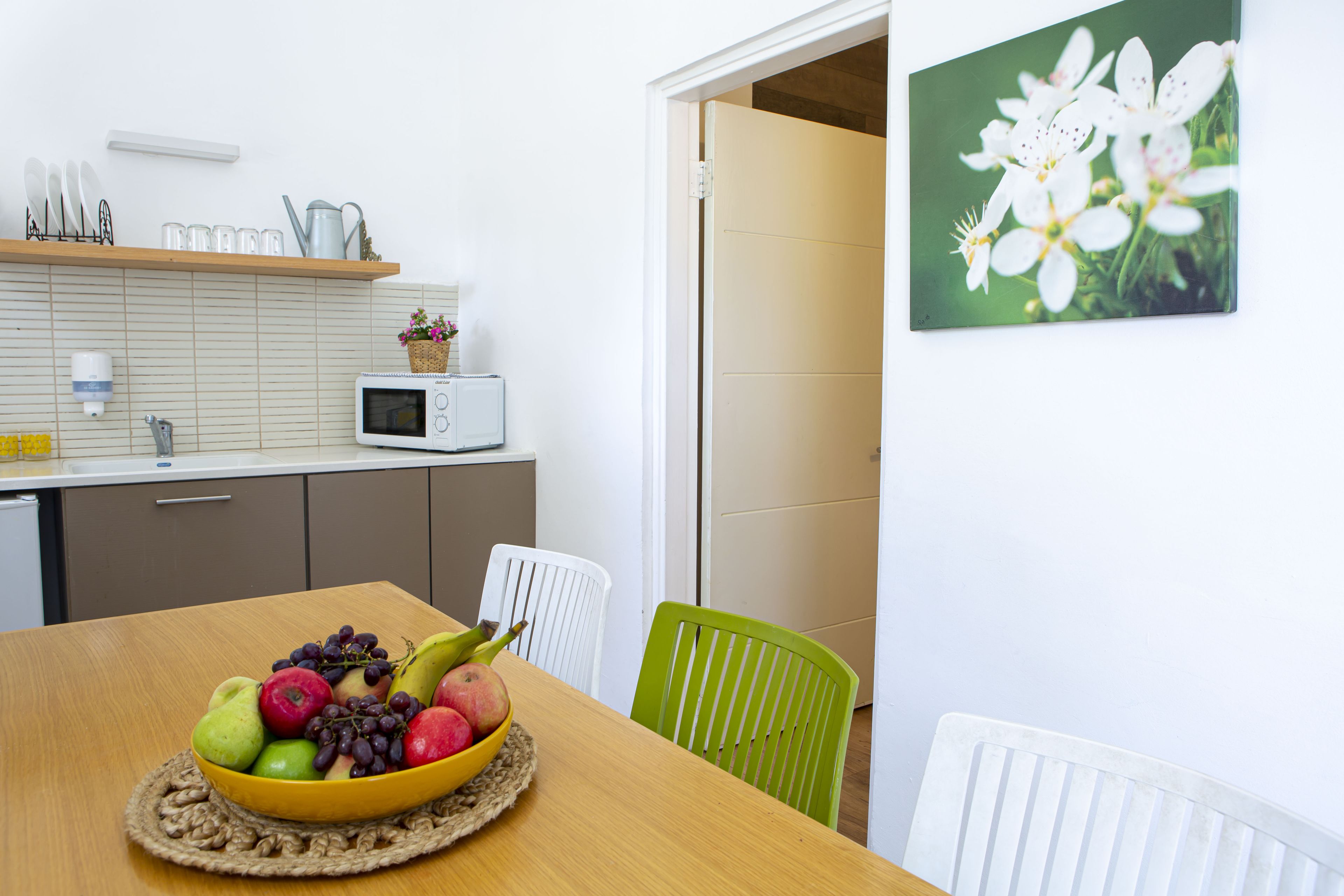 A kitchen with a microwave, a fruit bowl on the table, and a door leading to another room.