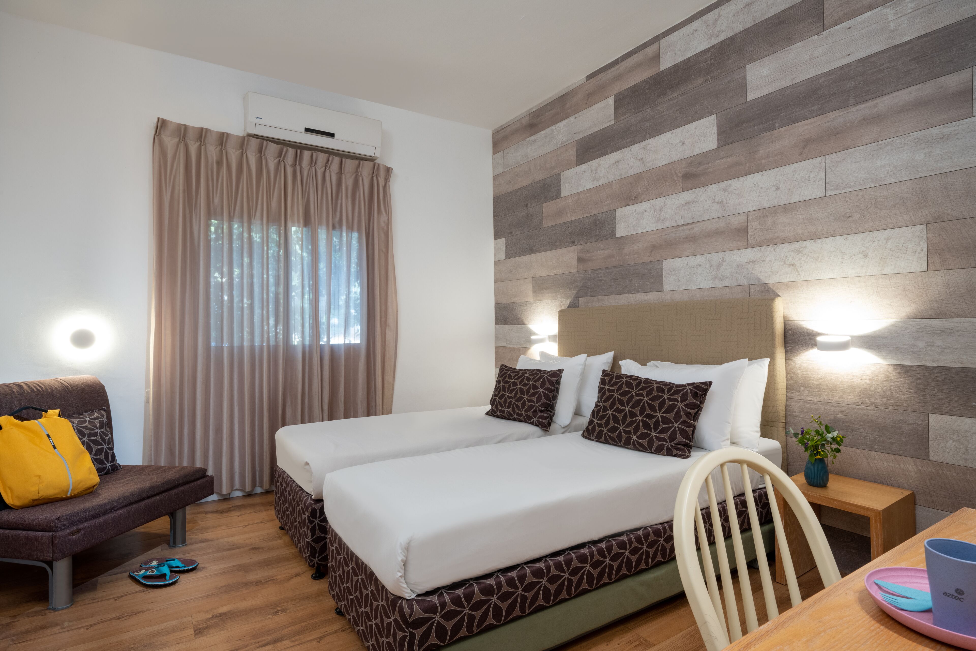 A hotel room with two beds, a sofa, a chair, a table, and an air conditioning unit.
