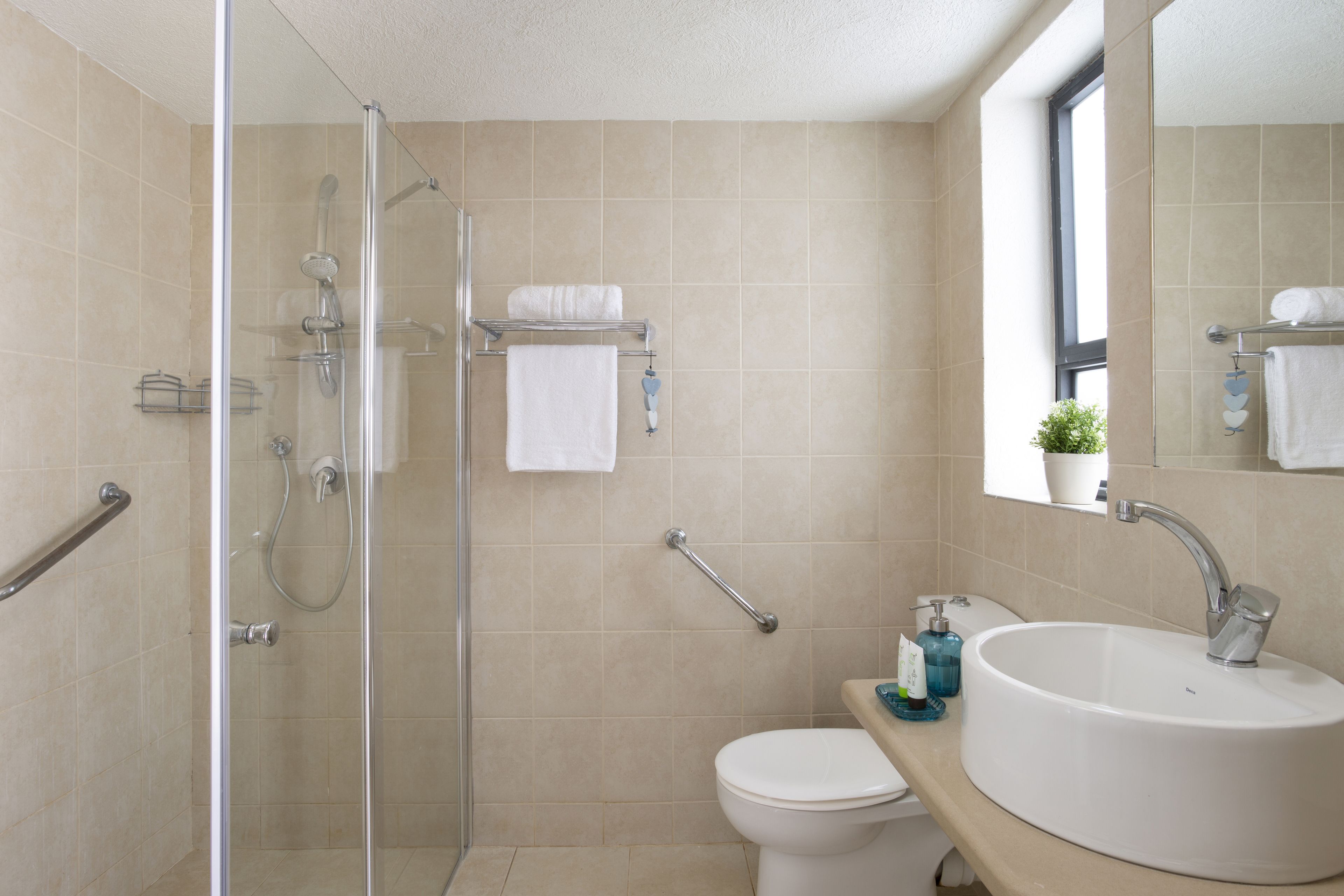 Un baño con cabina de ducha de vidrio, inodoro blanco y lavabo con espejo superior.
