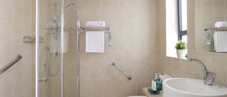 Un baño con cabina de ducha de vidrio, inodoro blanco y lavabo con espejo superior.