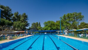 Piscina azul clara con separadores de carril, rodeada de árboles y zonas sombreadas.