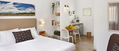 Une chambre d’hôtel moderne dotée d’un grand lit, d’un coin repas avec une table et des chaises, d’un four à micro-ondes et d’un petit coin cuisine.