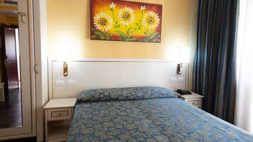 Ein Hotelzimmer mit einem großen Bett, zwei Nachttischen, einem Schminktisch, einem Gemälde von Sonnenblumen und einem Fenster mit Vorhängen.