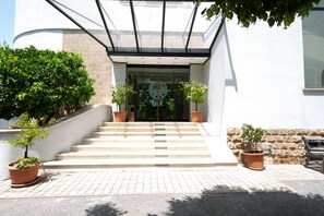 A building entrance with a staircase leading up to a glass door, flanked by potted plants. - Cervara Park Hotel (Rome)