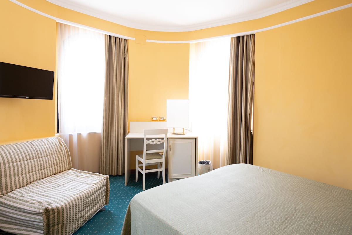 Ein Hotelzimmer mit Bett, Schreibtisch, Stuhl und Fernseher.