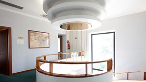 A modern interior with a circular wooden railing, a white wall with a framed painting, and a door leading to another room. - Cervara Park Hotel (Rome)