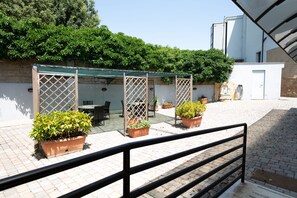 An outdoor patio area with a covered seating area, potted plants, and a brick floor. - Cervara Park Hotel (Rome)