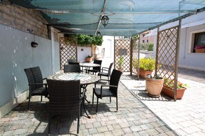 A patio area with a round table and chairs, a large potted plant, and a lattice partition. - Cervara Park Hotel (Rome)