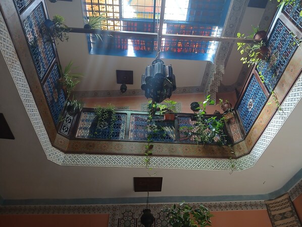 A multi-level interior with ornate metal railings, potted plants, and patterned wall tiles.