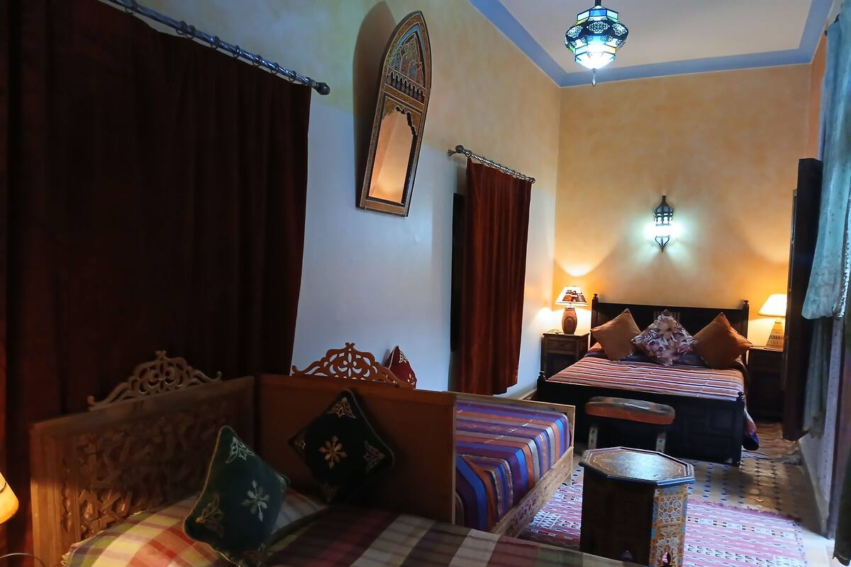 A cozy hotel room with two beds, a wooden headboard, a decorative mirror, and a patterned rug.